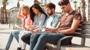 adults sitting on a park bench on smart phones | social media addiction