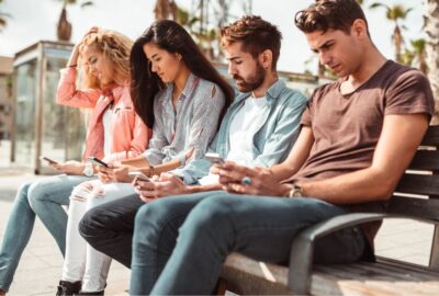 adults sitting on a park bench on smart phones | social media addiction