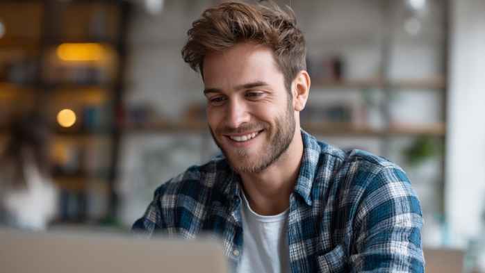 Guy looking at laptop smiling | confidence v. arrogance