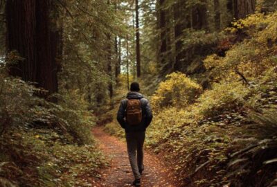 young black man walking off of a straight lined path onto another path while hiking in Northern California woods. | shortcut to success